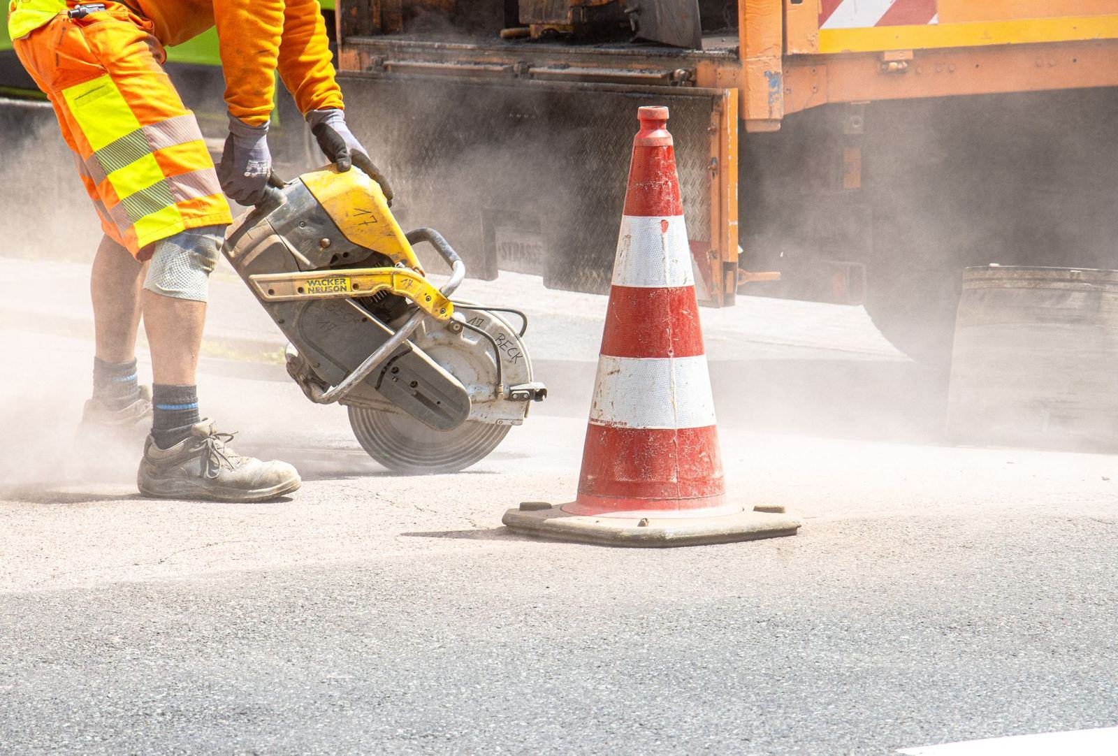 Worker saw-cutting pavement next to a traffic cone (stock photo)